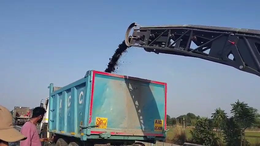Machine removing top layer of road and loading it in truck