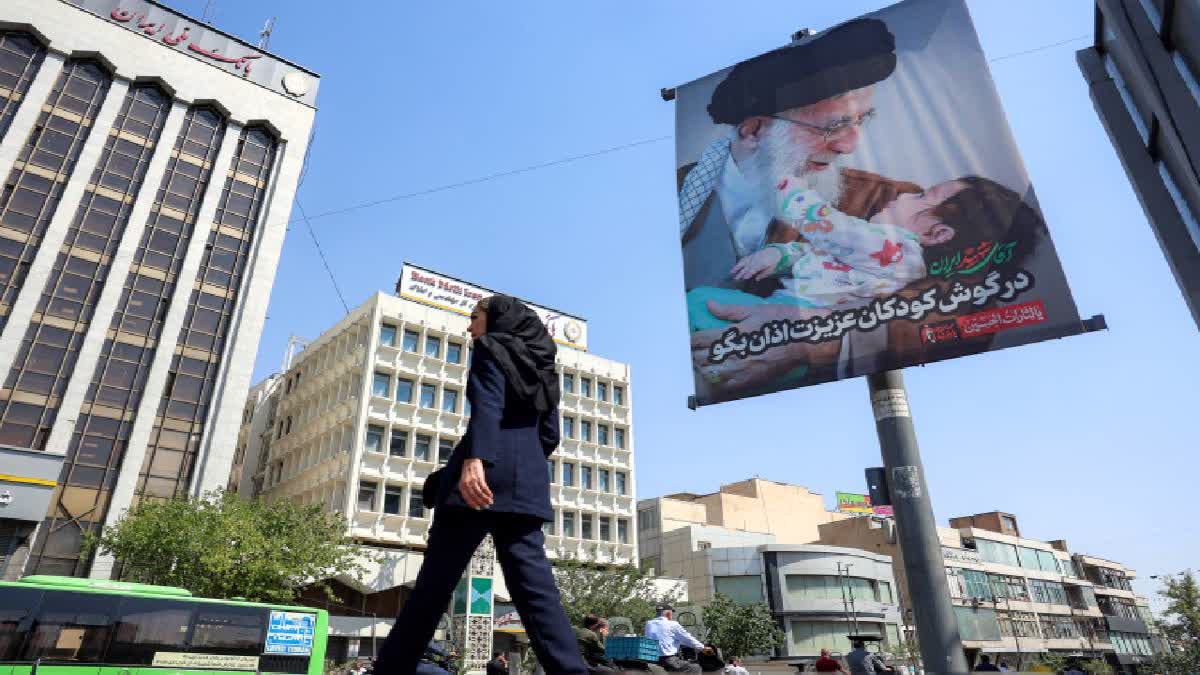 A woman crosses a road past a mourning billboard depicting Iran's slain supreme leader Ali Khamenei, who was killed in a strike on the first day of the US-Israeli war against the Iran on February 28, in Tehran on June 30, 2026 ahead of his public funeral.