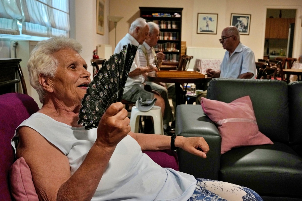 Jenny Sakellariou uses a hand fan while men play backgammon in an air-conditioned cooling center operated by the Athens municipality throughout a heat wave in Athens, Greece