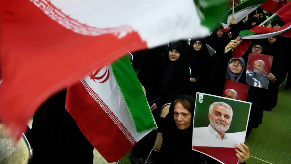 Women wave national flags as they hold up posters of the late commander of the Iran's Revolutionary Guard expeditionary Quds Force, Gen. Qassem Soleimani, who was killed in a U.S. drone attack in 2020 in Iraq, during a ceremony commemorating his death anniversary at the Imam Khomeini grand mosque in Tehran, Iran, Thursday, Jan. 1, 2026.