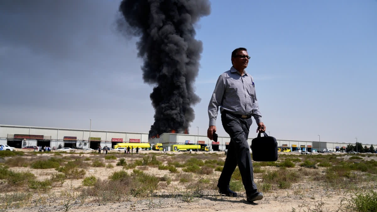 A man walks away after watching as a black plume of smoke rises from a warehouse in the industrial area of Sharjah City, United Arab Emirates, Sunday, March 1, 2026, following reports of Iranian strikes in Dubai.