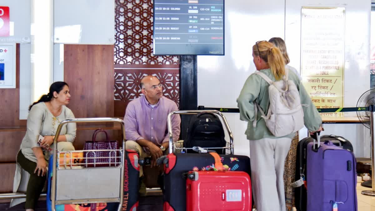Passengers wait below the flight information display at Cochin International Airport