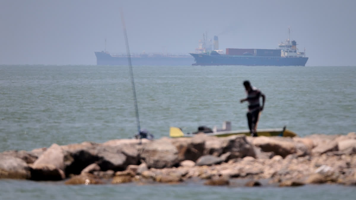 A man stands beside a fishing pole along the shore as cargo ships and commercial vessels are seen in the Strait of Hormuz off Bandar Abbas, Iran, Wednesday, June 17, 2026.