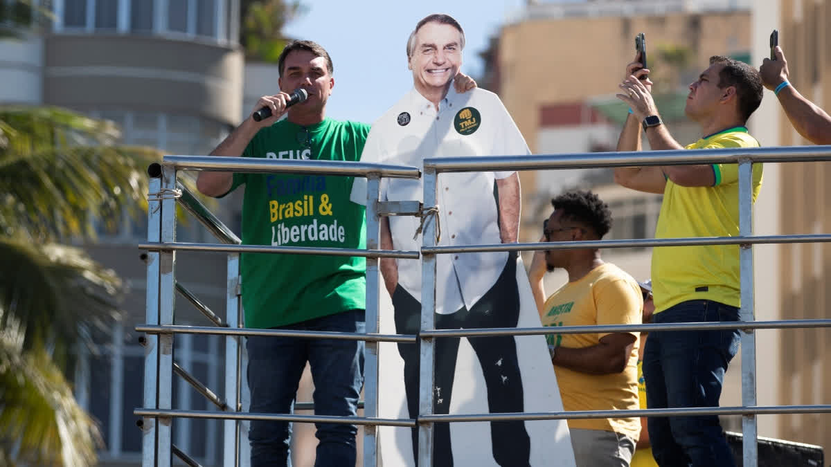 Senator Flavio Bolsonaro speaks while embracing a cutout of his father, former President Jair Bolsonaro, during a demonstration to protest a Supreme Court trial in which Jair Bolsonaro faces charges for alleged involvement in a 2022 coup attempt, at Copacabana Beach in Rio de Janeiro, Sunday, Aug. 3, 2025.