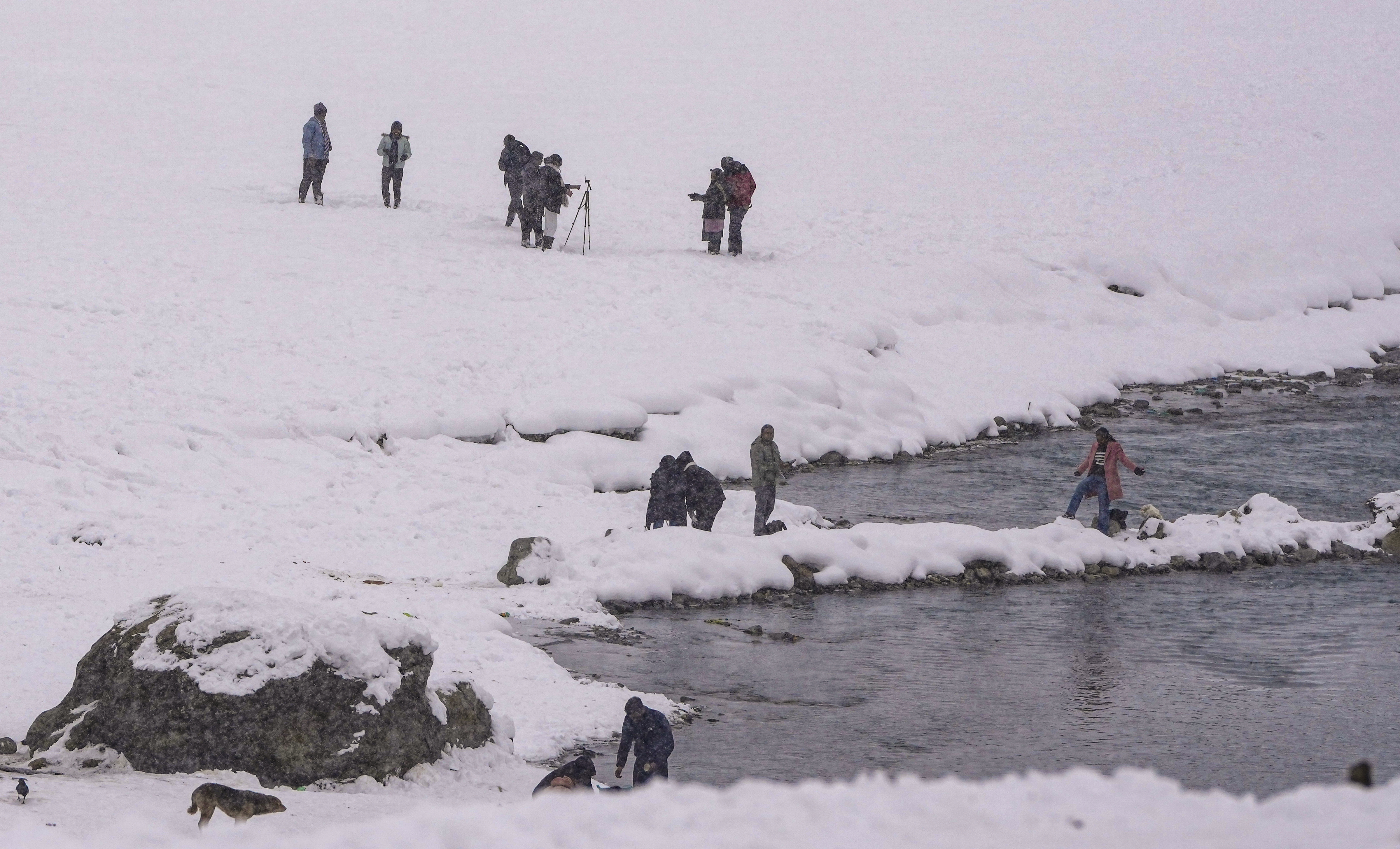 Tourists and photographers capture light snowfall along a stream amid a snow-covered landscape, in Sonamarg, Jammu and Kashmir