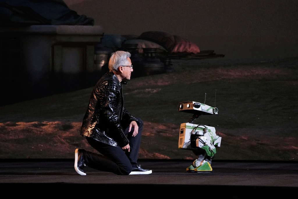 Nvidia founder and CEO Jensen Huang kneels in front of a robot during a Nvidia news conference ahead of the CES tech show Monday, Jan. 5, 2026, in Las Vegas