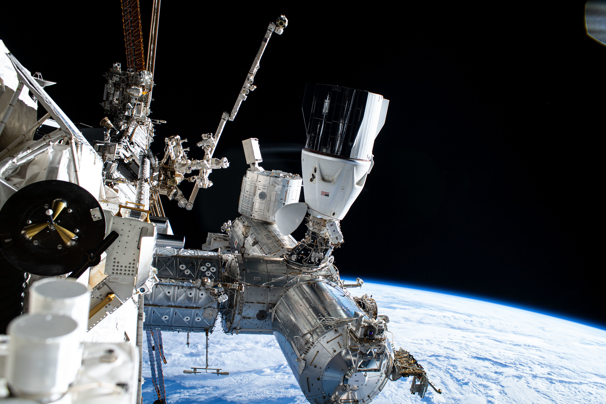 File Photo: NASA astronaut and Expedition 72 Commander Suni Williams (center) is dwarfed near the SpaceX Dragon crew spacecraft as she replaces a planar reflector, advanced navigational hardware visiting vehicles use when approaching the International Space Station.