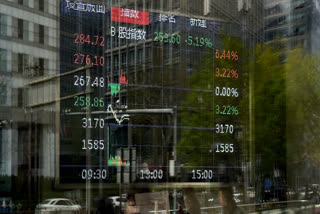 Pedestrian are reflected on a brokerage house's window as an electronic board displays shares trading index, in Beijing, Monday, April 7, 2025.