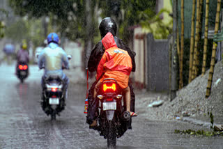 A man rides a motorcycle with a child during rain, in Siliguri, West Bengal, on Tuesday.
