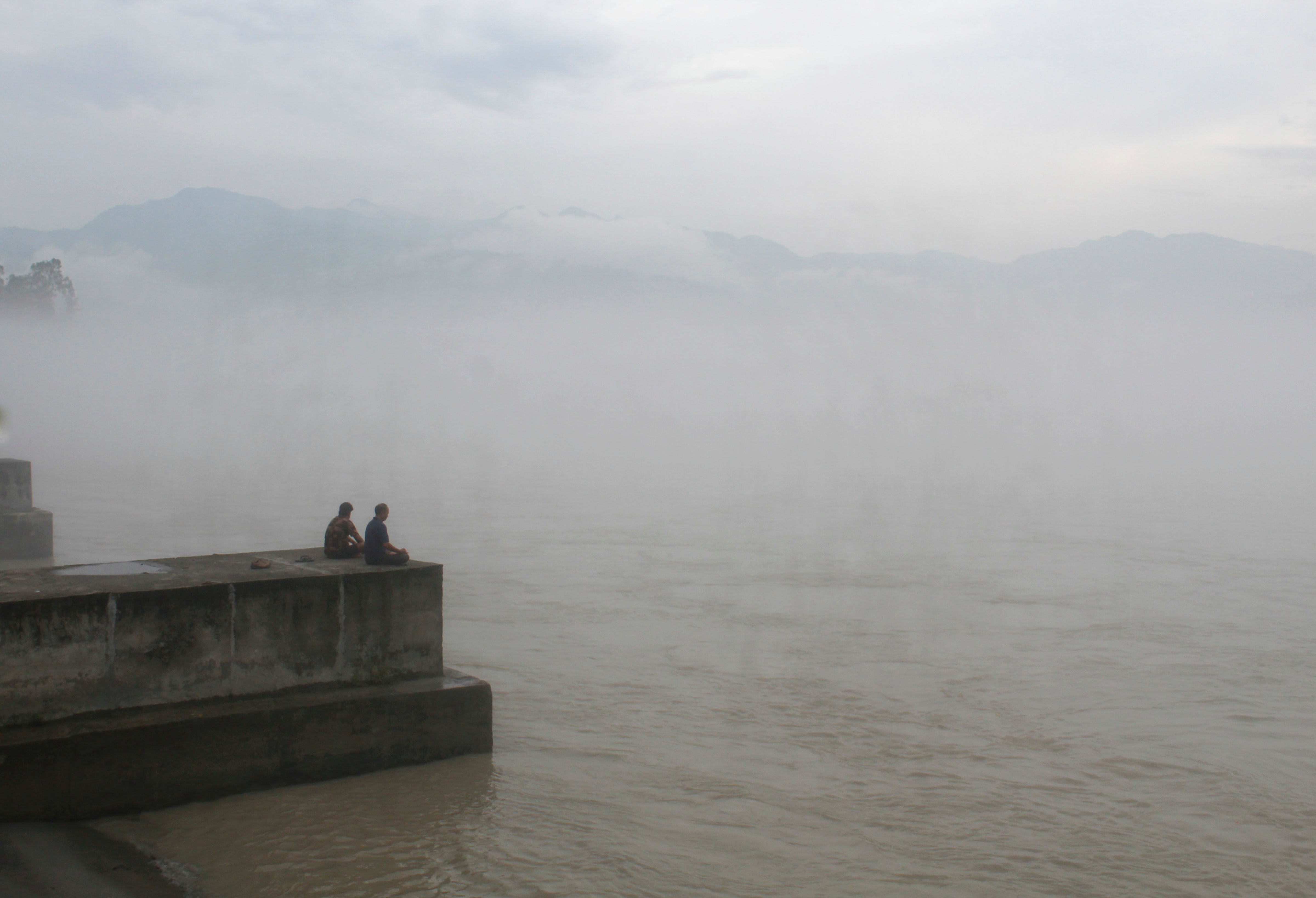 Two men sit on a riverside platform overlooking the Ganga as thick monsoon clouds partially obscure the surrounding mountains after rainfall, in Rishikesh, on Wednesday.