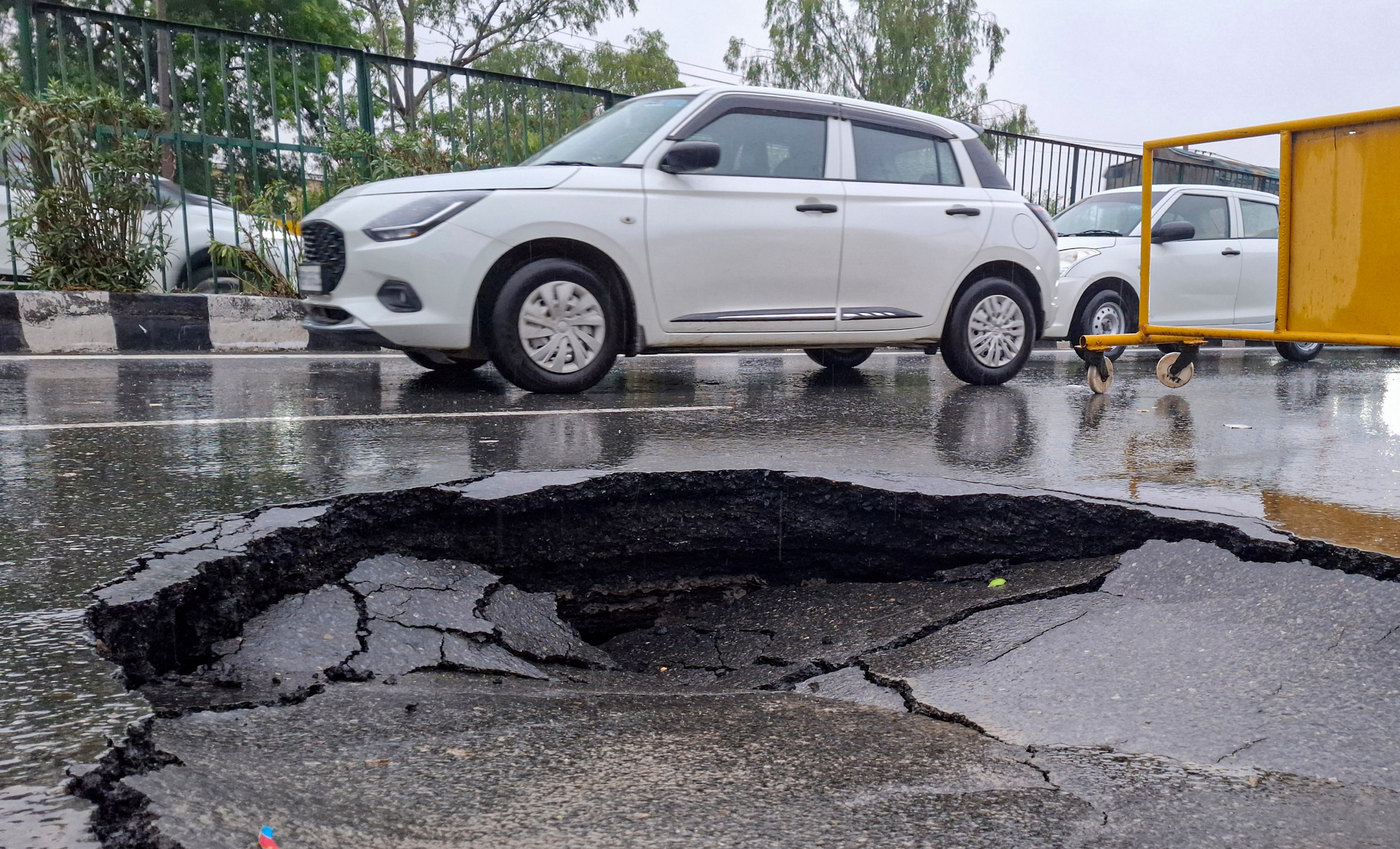 Vehicles move near a caved-in section of a road following monsoon rains, in Gurugram.
