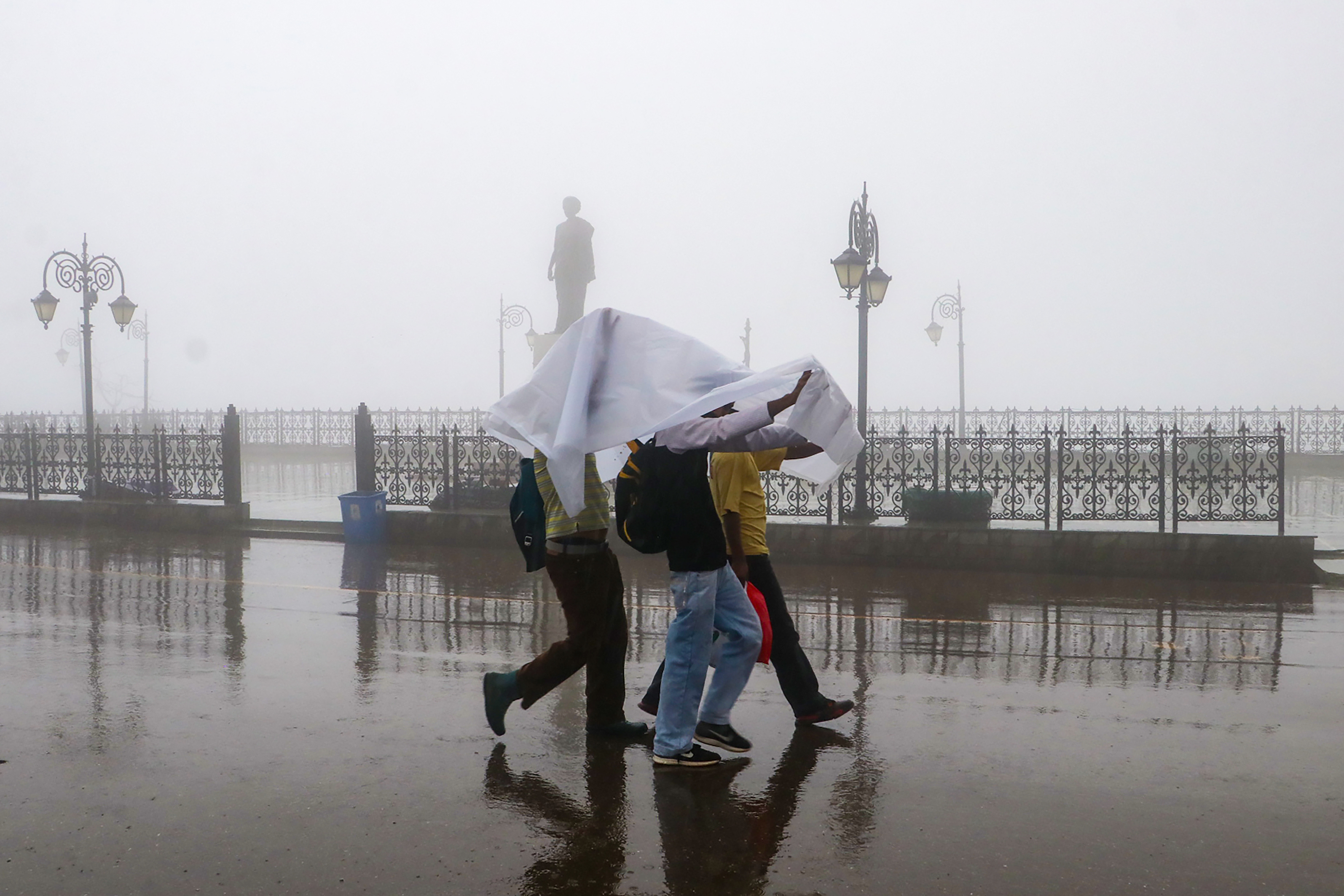 People cover themselves with cloth to shield from the rain as they walk across the Ridge Maidan amid dense fog and heavy rain in Shimla on Wednesday.