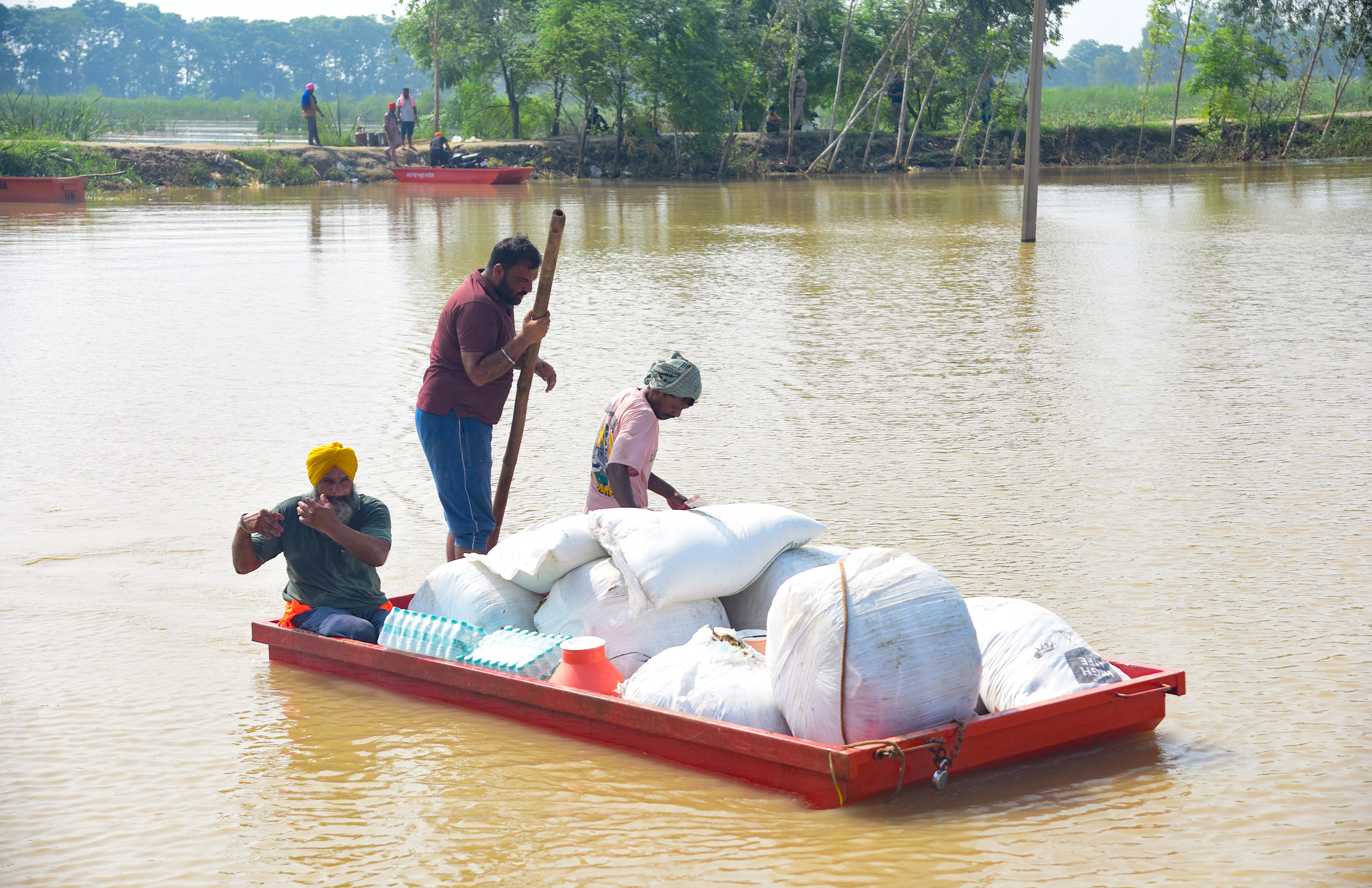 Volunteers transport relief material by boat through floodwaters of the Beas River at Baoopur village, in Kapurthala district of Punjab.