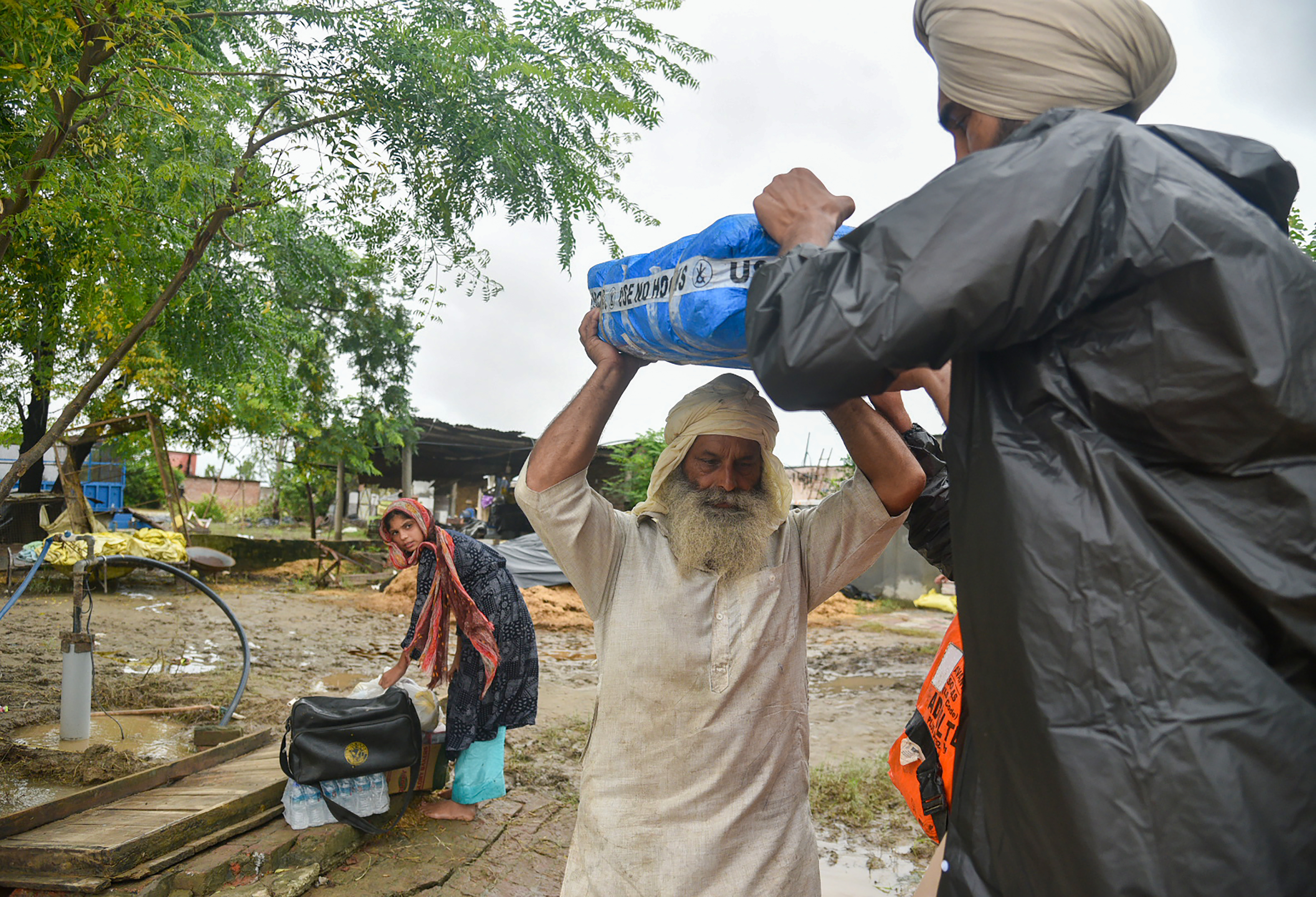 Local residents carry water and food for distribution to stranded people through the flooded waters of the Beas River at Mand village in Kapurthala district of Punjab.
