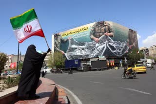 A woman holds Iran’s national flag while standing near a billboard with a sentence reading ‘The Strait of Hormuz remains closed’ at the Enqelab Square in Tehran, on April 5, 2026.