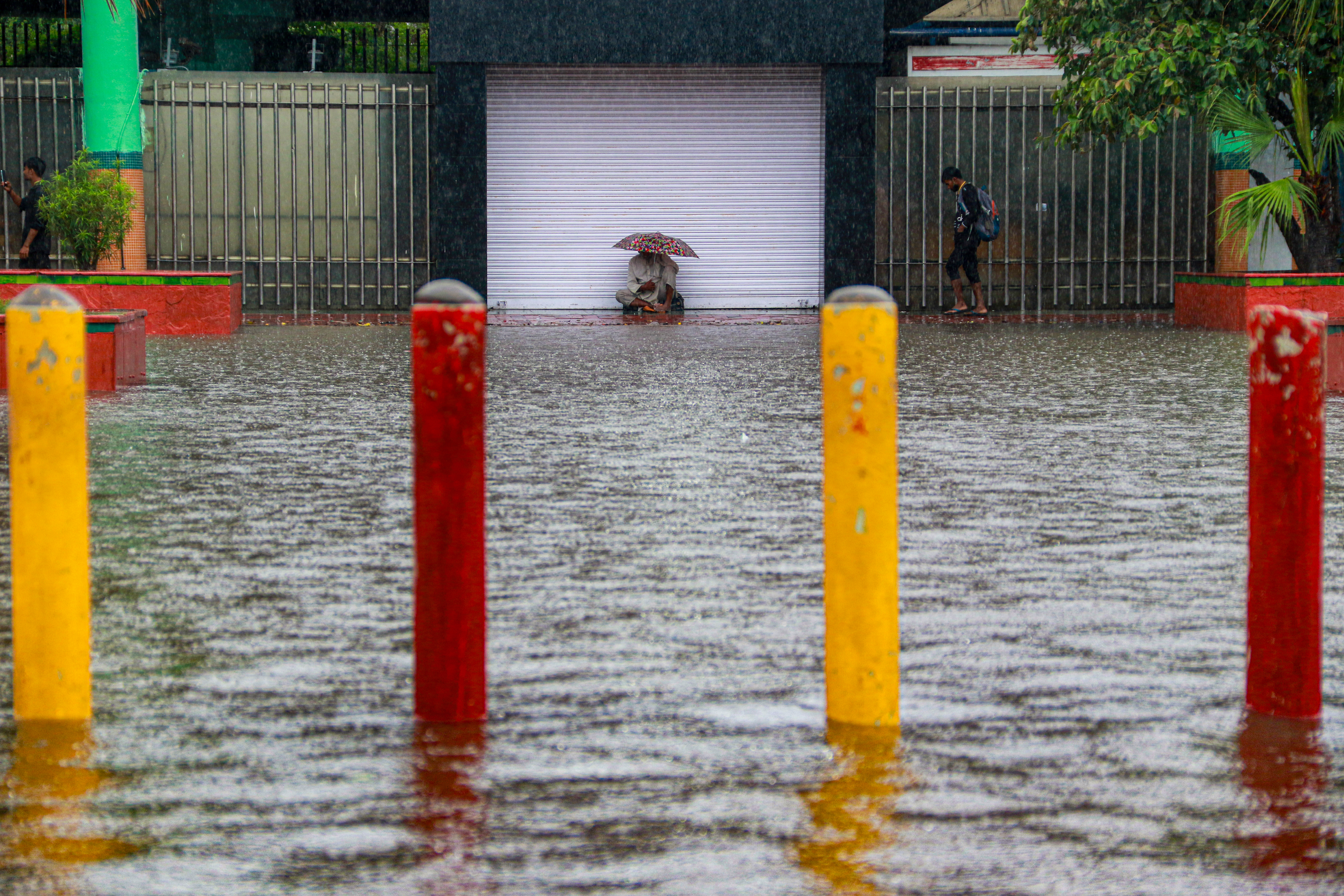 A man holding an umbrella takes shelter by the roadside during rainfall in New Delhi on Thursday.