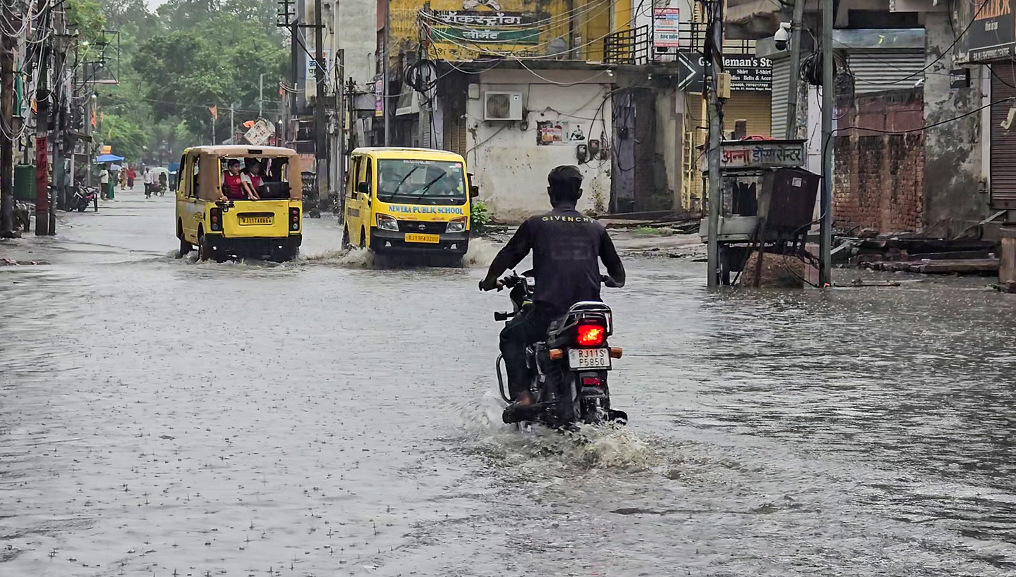 Commuters make their way through a waterlogged road caused by heavy rainfall in Dholpur.