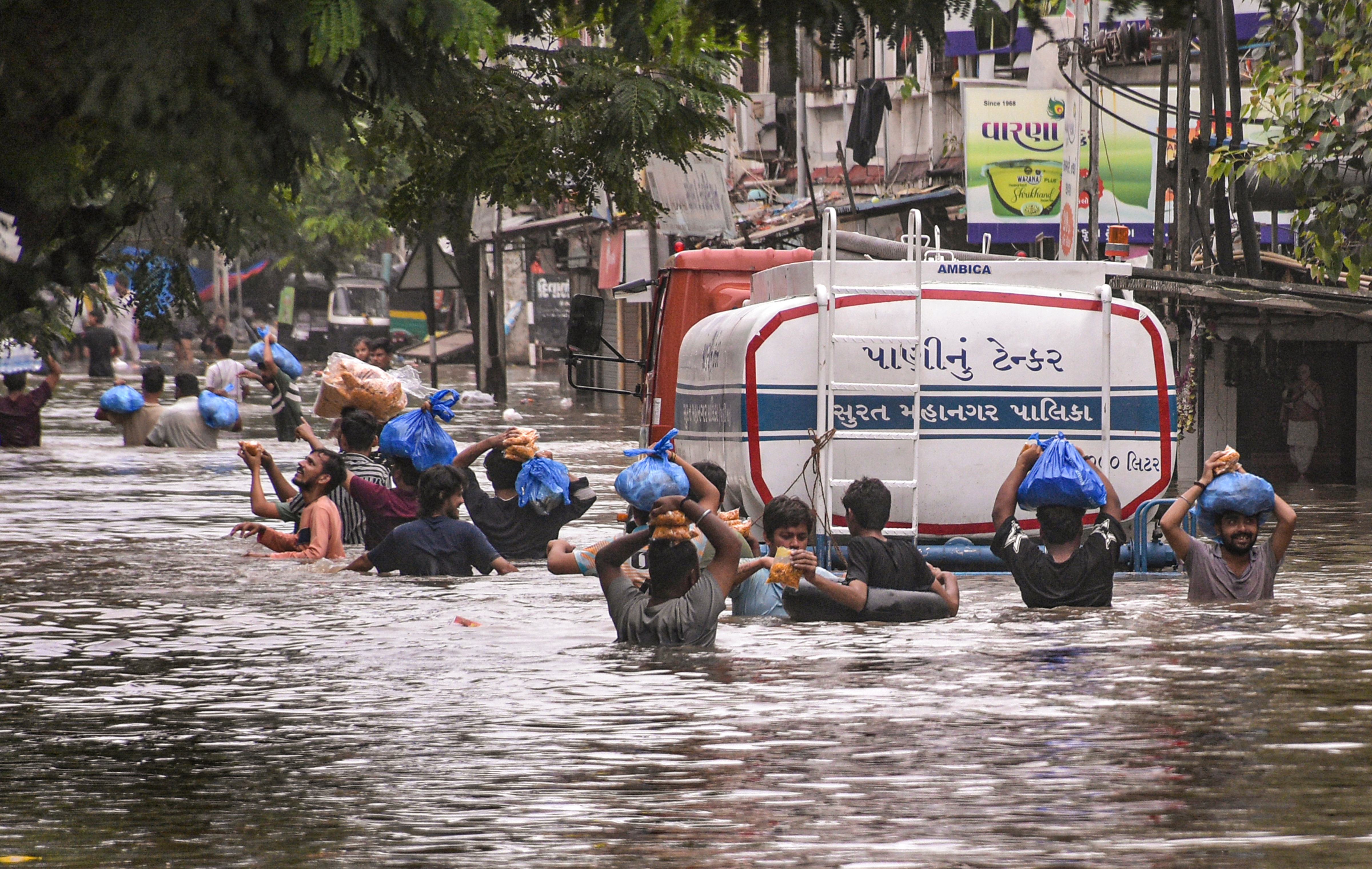 People carry packets of food items on their heads as they wade through a waterlogged road after heavy rain, in Surat.