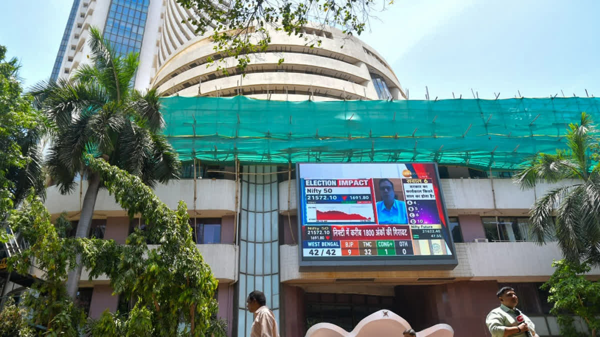 Sensex Rises 323 Pts, Nifty Rallies For 6th Day Amid Optimism Over US-India Trade Talks People walk past a screen showing stock market goes down outside BSE building at Dalal Street after the counting of votes for Lok Sabha polls, in Mumbai on Tuesday, June 4, 2024.