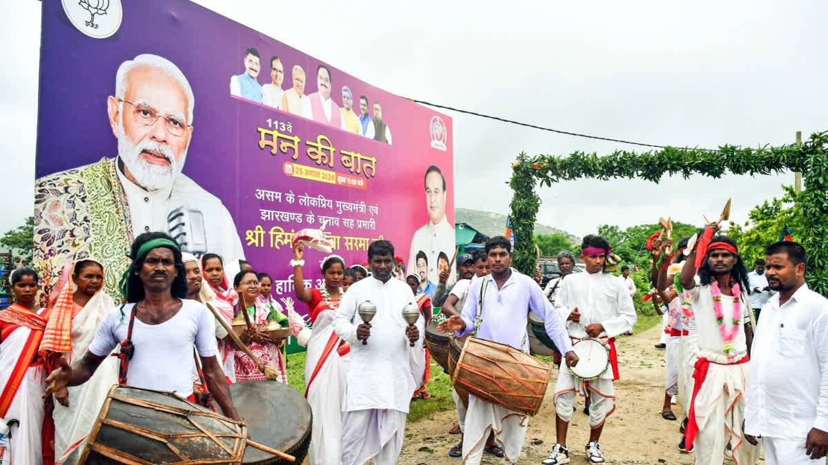 File | Members of tribal community playing drums in front of banner of Prime Minister Narendra Modi.