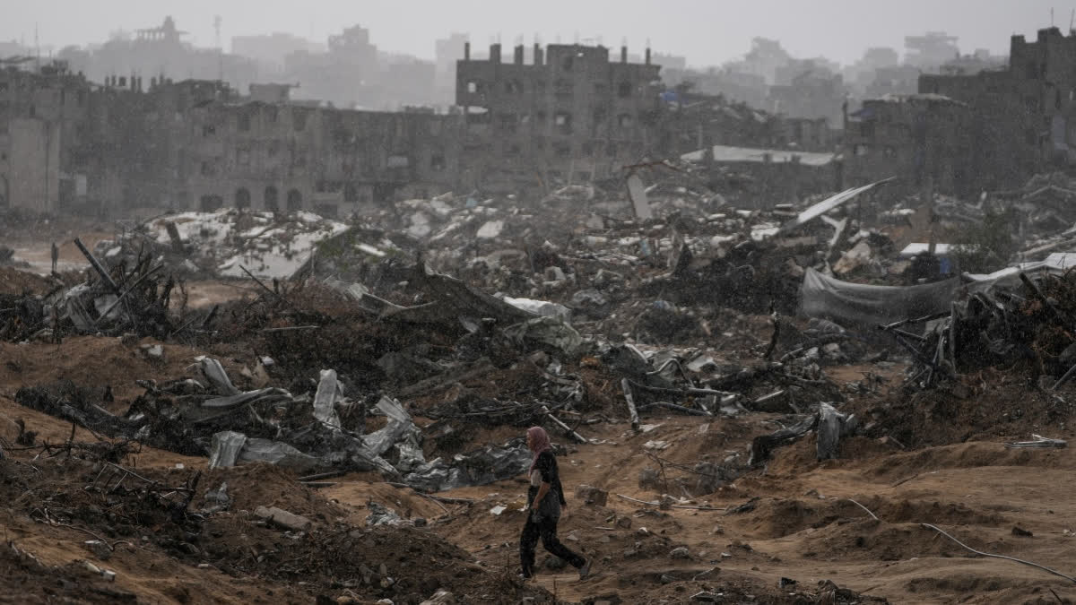 A Palestinian woman walks through a rainstorm past buildings destroyed in Israeli strikes in the Sheikh Radwan neighborhood of Gaza City, Friday, Nov. 14, 2025.