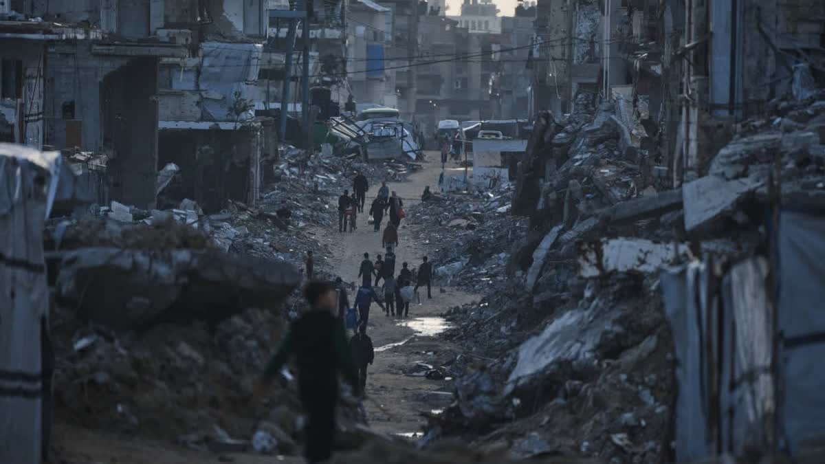 Palestinians walk amid buildings destroyed by Israeli air and ground operations in Gaza City Thursday, Jan. 15, 2026
