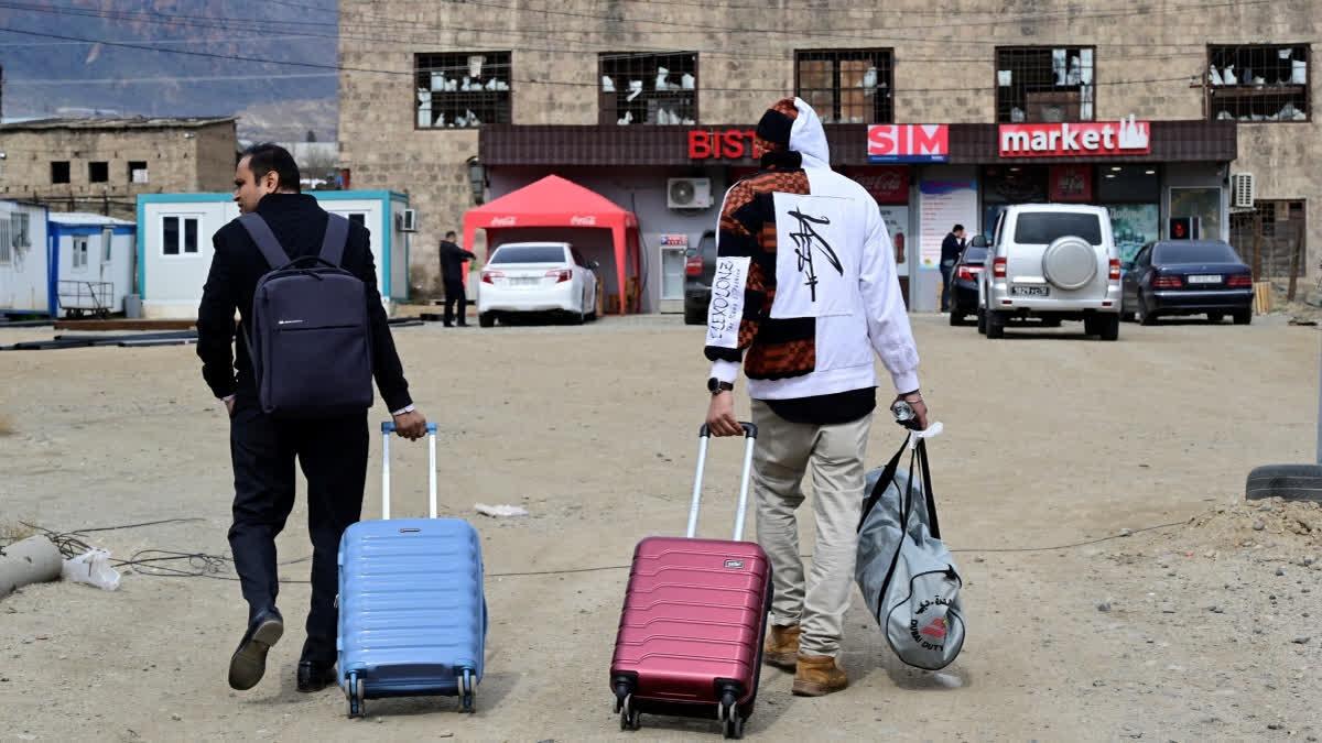 Iranian refugees walk with their belongings after crossing the border from Iran to Armenia at a border check point in the southern Armenian town of Meghri, on March 9, 2026, amid the Middle East war.