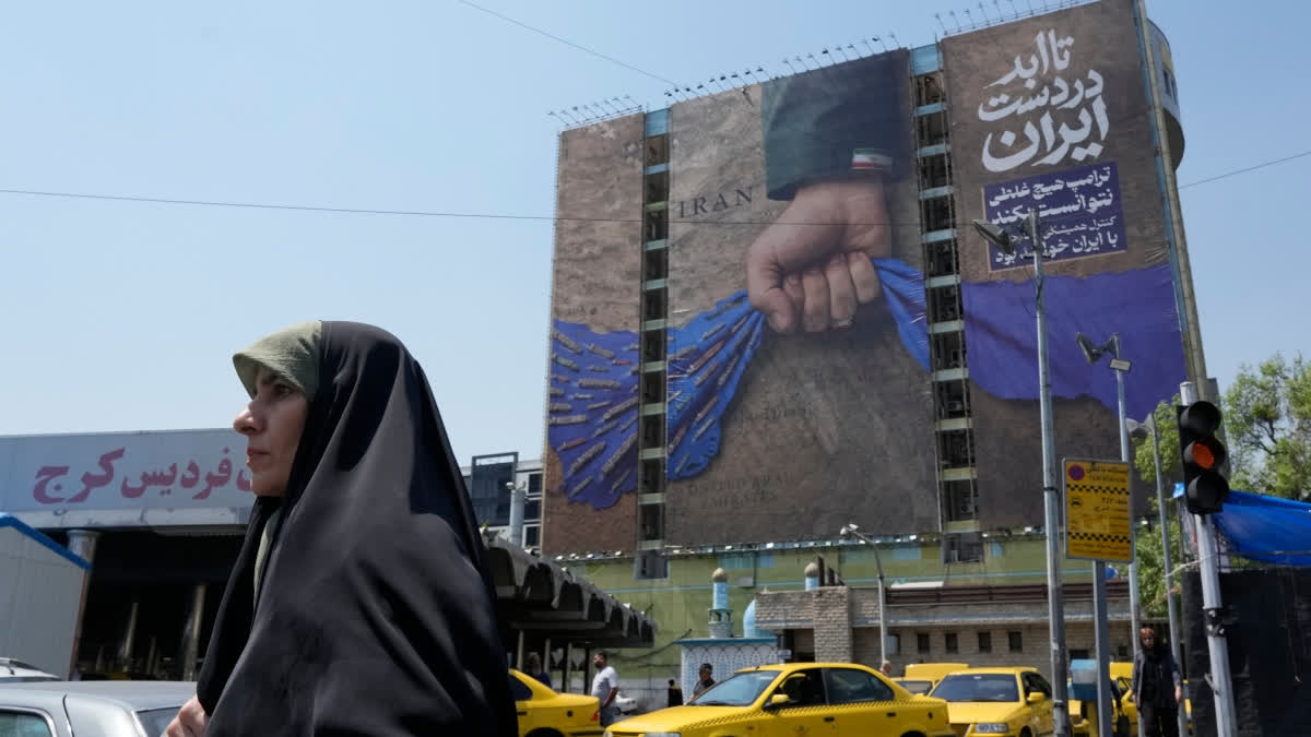 A woman walks past a billboard that shows a graphic depicting a military personnel's hand holding the Strait of Hormuz in his fist with signs which read in Farsi: "In Iran's hands forever," "Trump couldn't do a damn thing," " The control of Strait of Hormuz will be Iran's forever," in Vanak Square, in northern Tehran, Iran, Thursday, April 16, 2026.