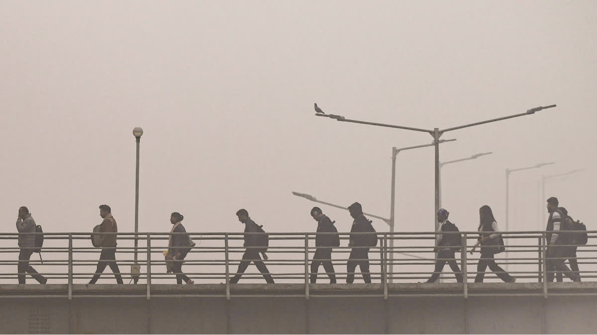 Commuters walk across a foot-over bridge amid dense fog on a winter morning, near Akshardham Temple, in New Delhi, Friday