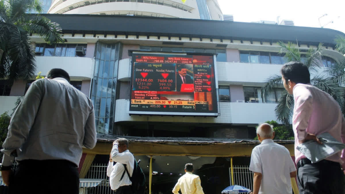 FILE- People look at a screen displaying the current market situation on the facade of the Bombay Stock Exchange (BSE), in Mumbai.