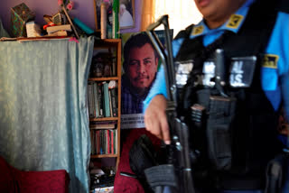 FILE - A poster of slain environmentalist Juan López hangs in his home as a state-assigned bodyguard watches over the López family, in Tocoa, Honduras, Dec. 6, 2024.