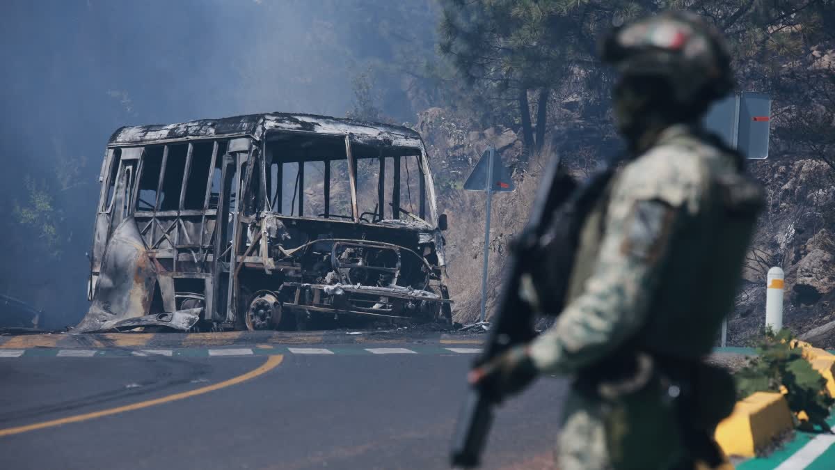 A soldier stands guard by a charred vehicle after it was set on fire, in Cointzio, Michoacán state, Mexico, Sunday, Feb. 22, 2026, following the death of the leader of the Jalisco New Generation Cartel, Nemesio Oseguera, known as "El Mencho."