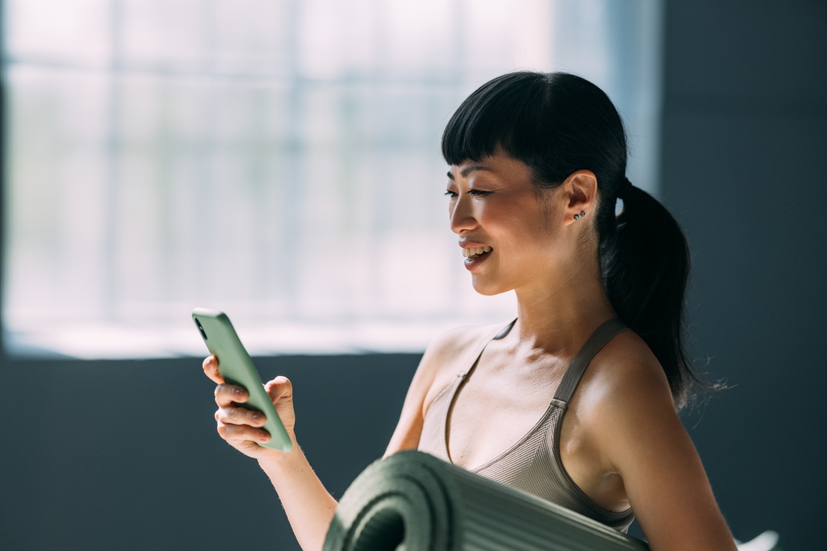 Woman with yoga mat looking at her phone