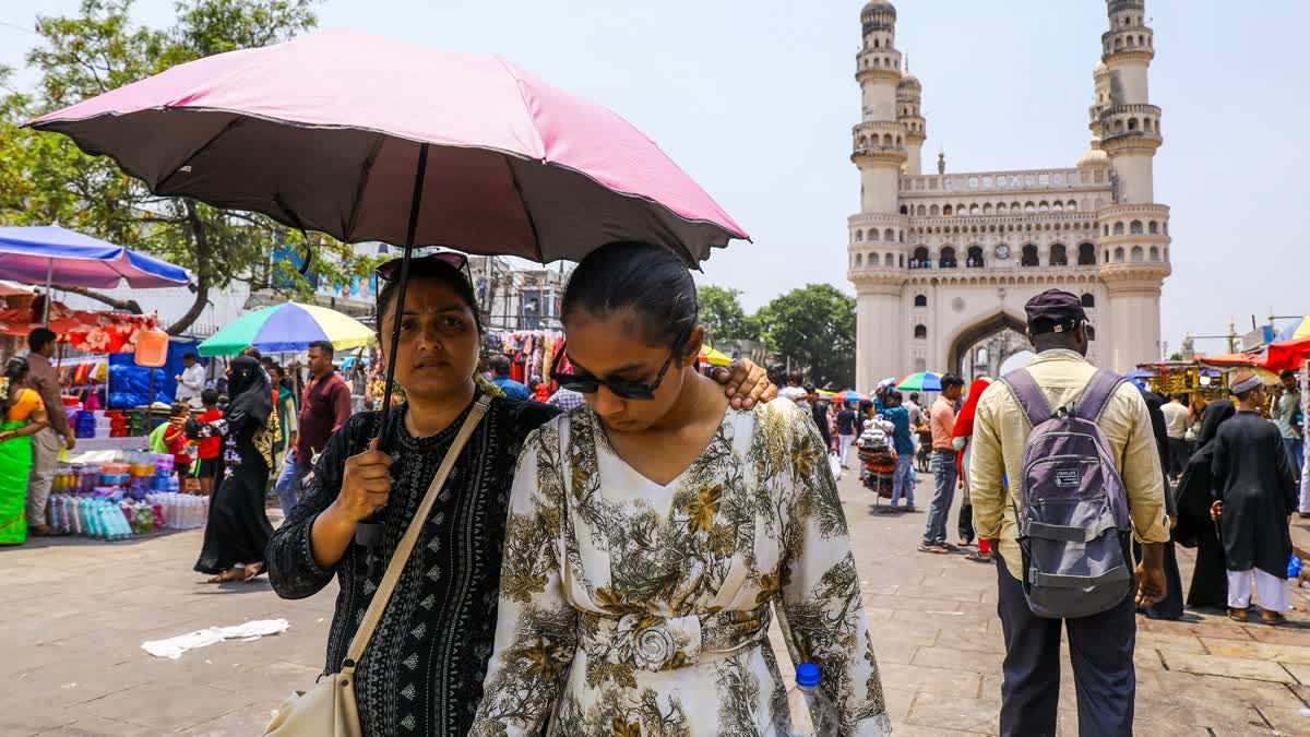 People explore the bustling market near Charminar while shielding themselves with umbrellas from the scorching summer heat on a hot afternoon in the Old City area of Hyderabad