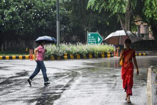 नवी दिल्लीमध्ये पावसापासून संरक्षण करण्यासाठी छत्री घेऊन जाणाऱ्या महिला
