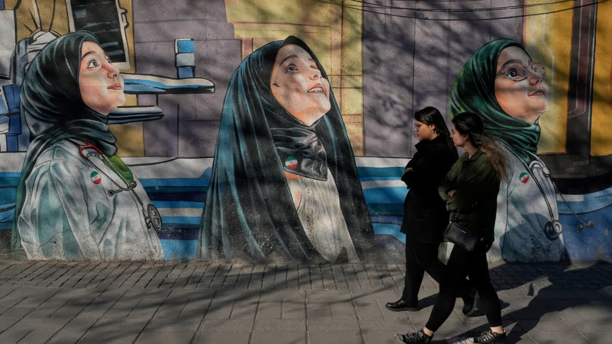 Women walk past a mural at a girls school at Enqelab-e-Eslami, or Islamic Revolution Street in downtown Tehran, Iran, Wednesday,