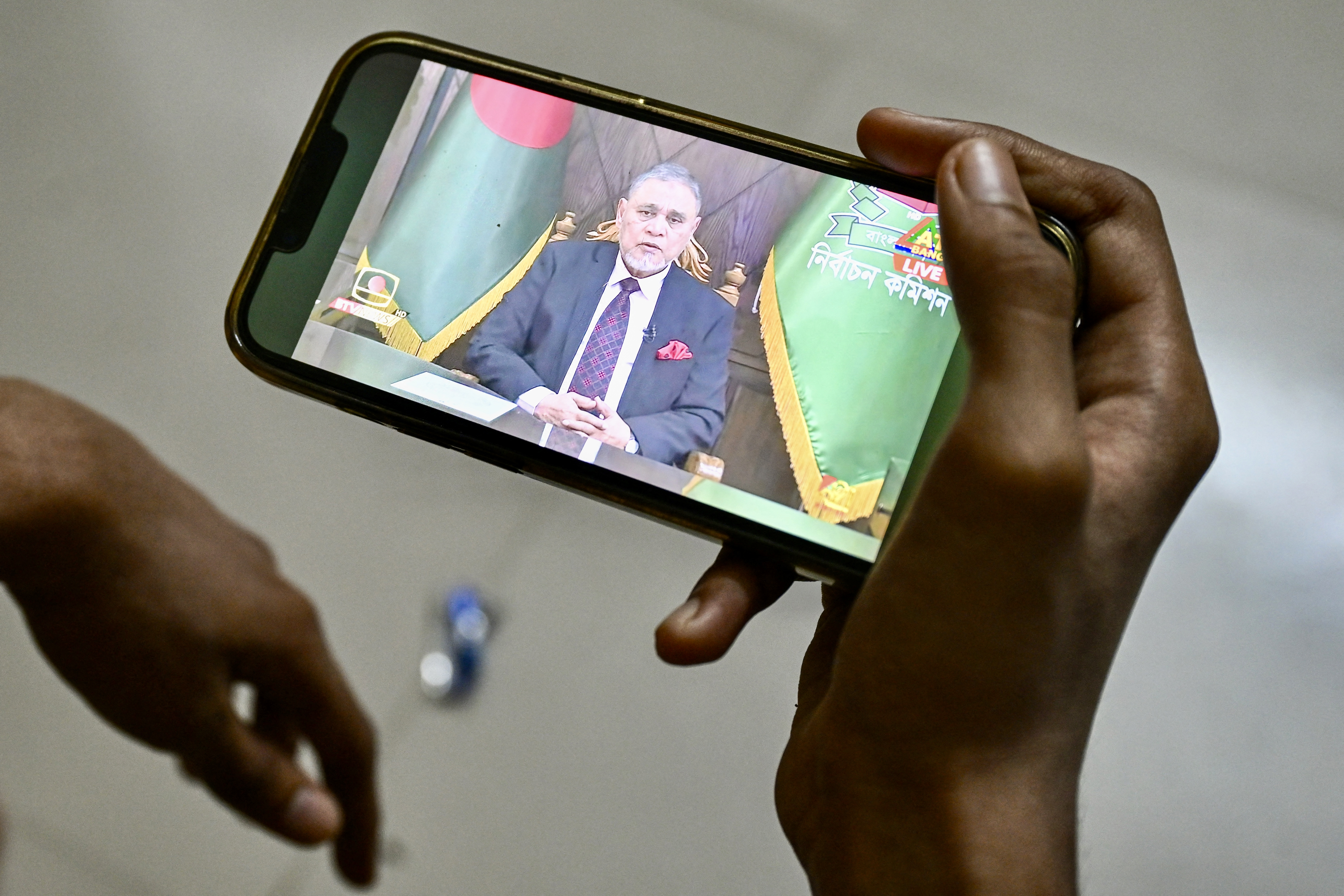 A man watches Chief Election Commissioner A. M. M. Nasir Uddin's address on mobile in Dhaka on December 11, 2025, during the announcement of the parliamentary elections and the July National Charter referendum. Bangladesh will hold national polls on February 12, the electoral commission announced on December 11, the country's first vote since a student-led uprising toppled former prime minister Sheikh Hasina last year.