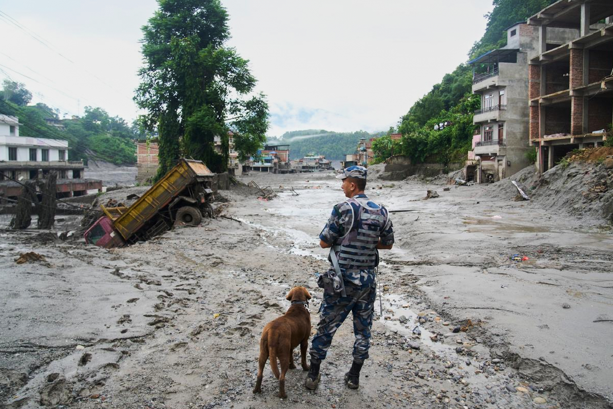 A policeman with a sniffer dog looks at the damage in the aftermath of flash floods in Nuwakot district.