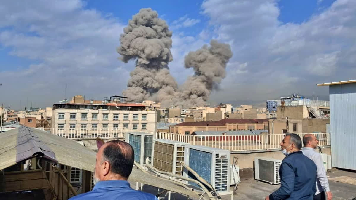 People watch as smoke rises on the skyline after an explosion in Tehran, Iran