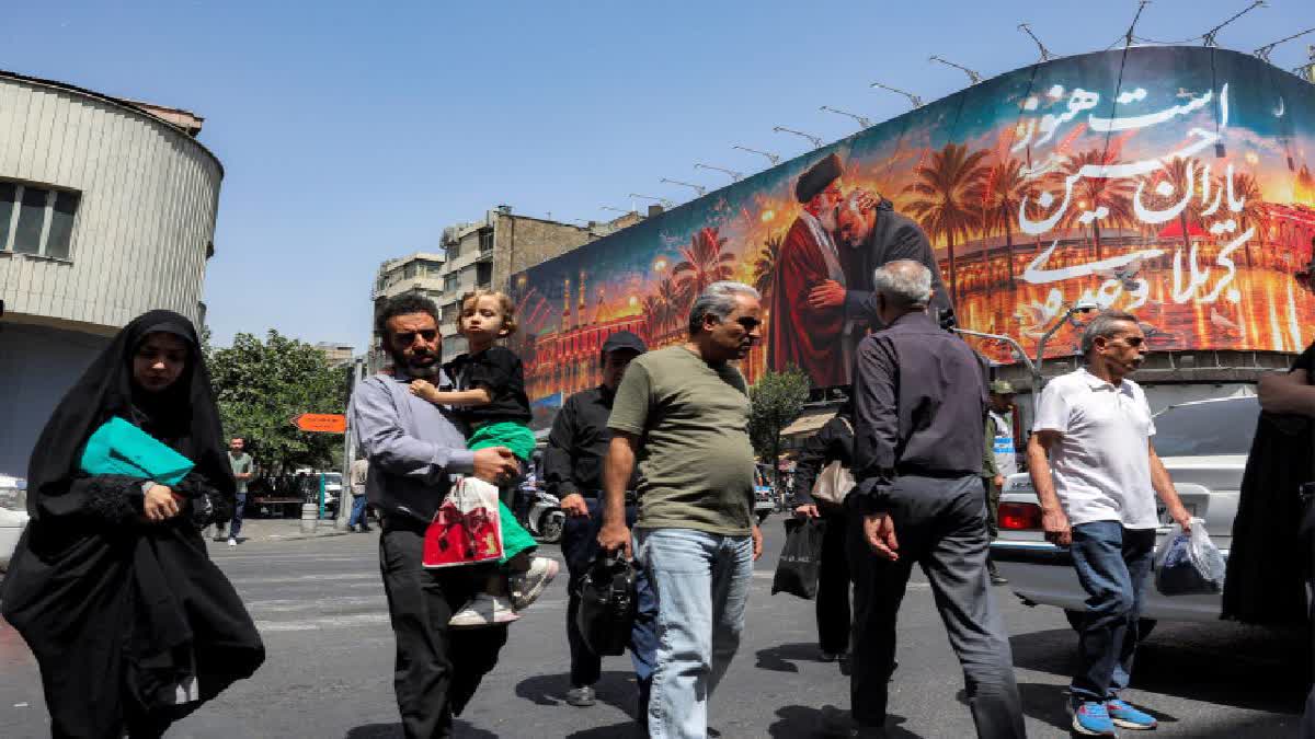 People cross a street past a billboard depicting Iran's slain supreme leader Ali Khamenei kissing the slain Islamic revolutionary guards commander Qasem Soleimani near the shrine of Imam Hussein Iraq's holy city of Karbala, displayed on the facade of a building in Tehran on June 29, 2026.